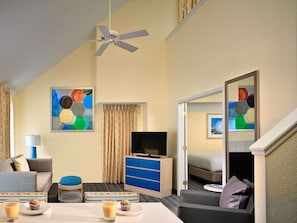 A hotel room with a ceiling fan, a flat-screen TV, a bed, a dining area with a table and chairs, and artwork on the walls. - Sonesta ES Suites St. Louis - Chesterfield (Chesterfield)