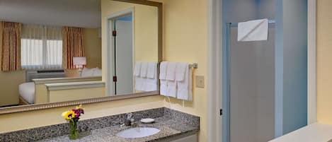 Ein Hotelbad mit Granitwaschtisch, Waschbecken, Spiegel und Duschbereich.