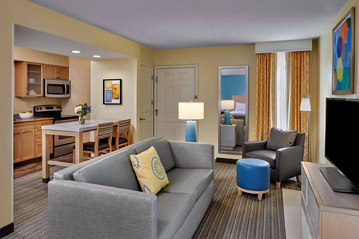 Une chambre d’hôtel comprenant un coin salon, une kitchenette et une chambre à coucher accessible par une porte.
