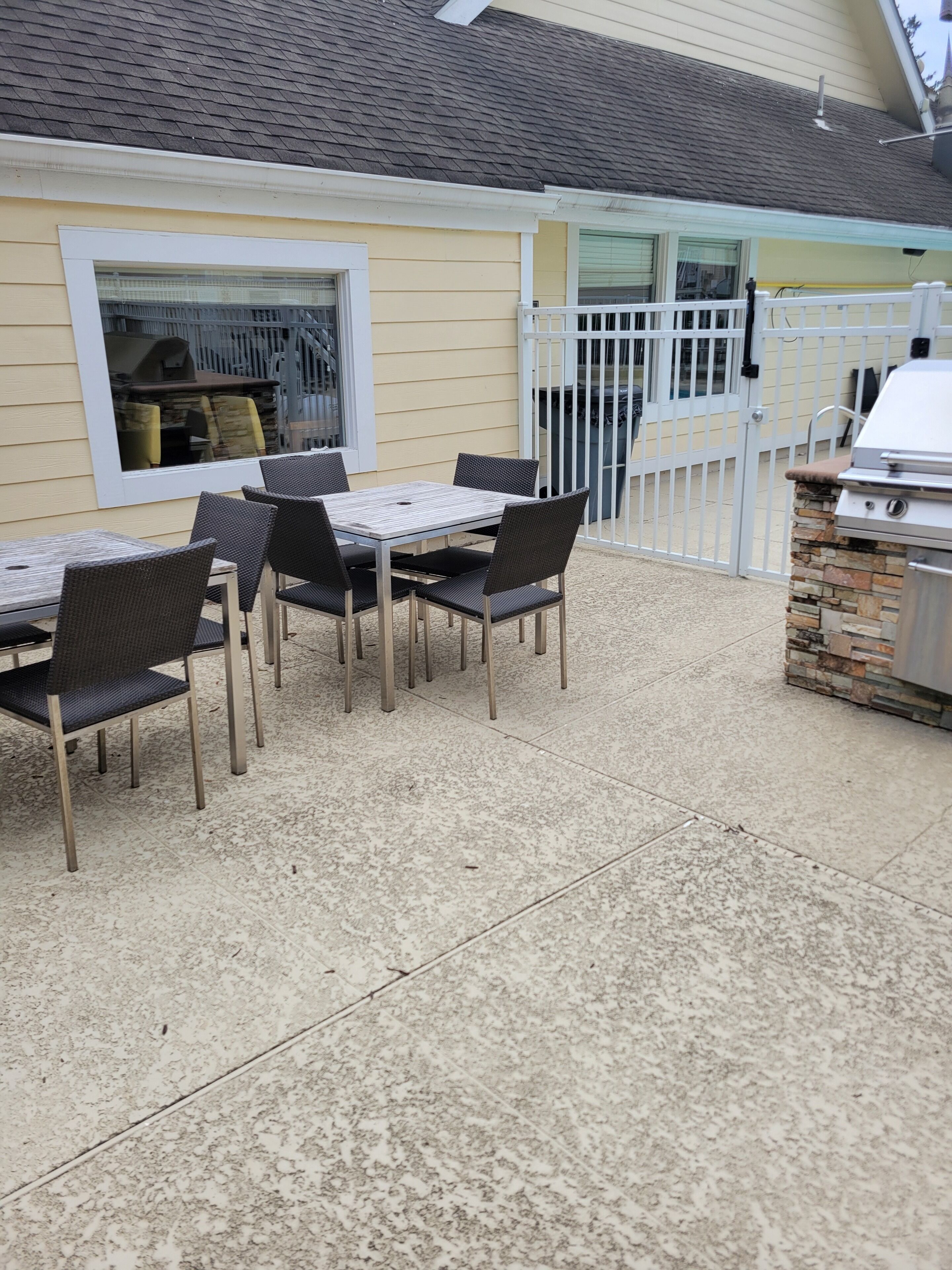 An outdoor patio with a table and chairs, a grill, and a gated entrance.