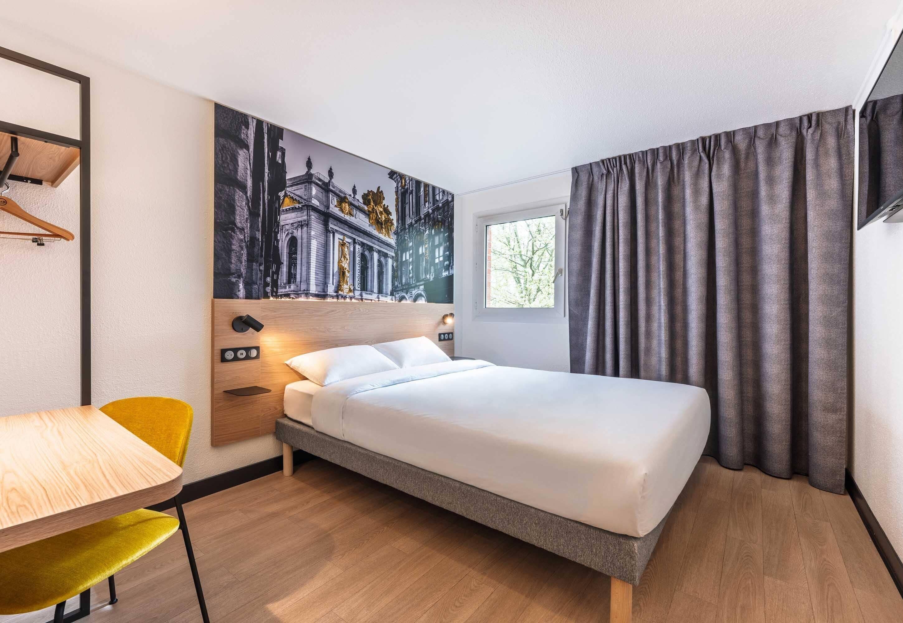 Ein Hotelzimmer mit Bett, Schreibtisch, Stuhl, einem Gemälde und einem Fenster mit Vorhängen.