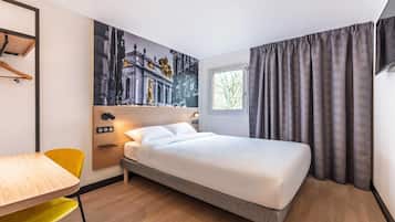 Ein Hotelzimmer mit Bett, Schreibtisch, Stuhl, einem Gemälde und einem Fenster mit Vorhängen.
