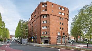 A multi-story hotel with a red brick facade, a ground floor with a visible entrance, and a red bike lane in front.