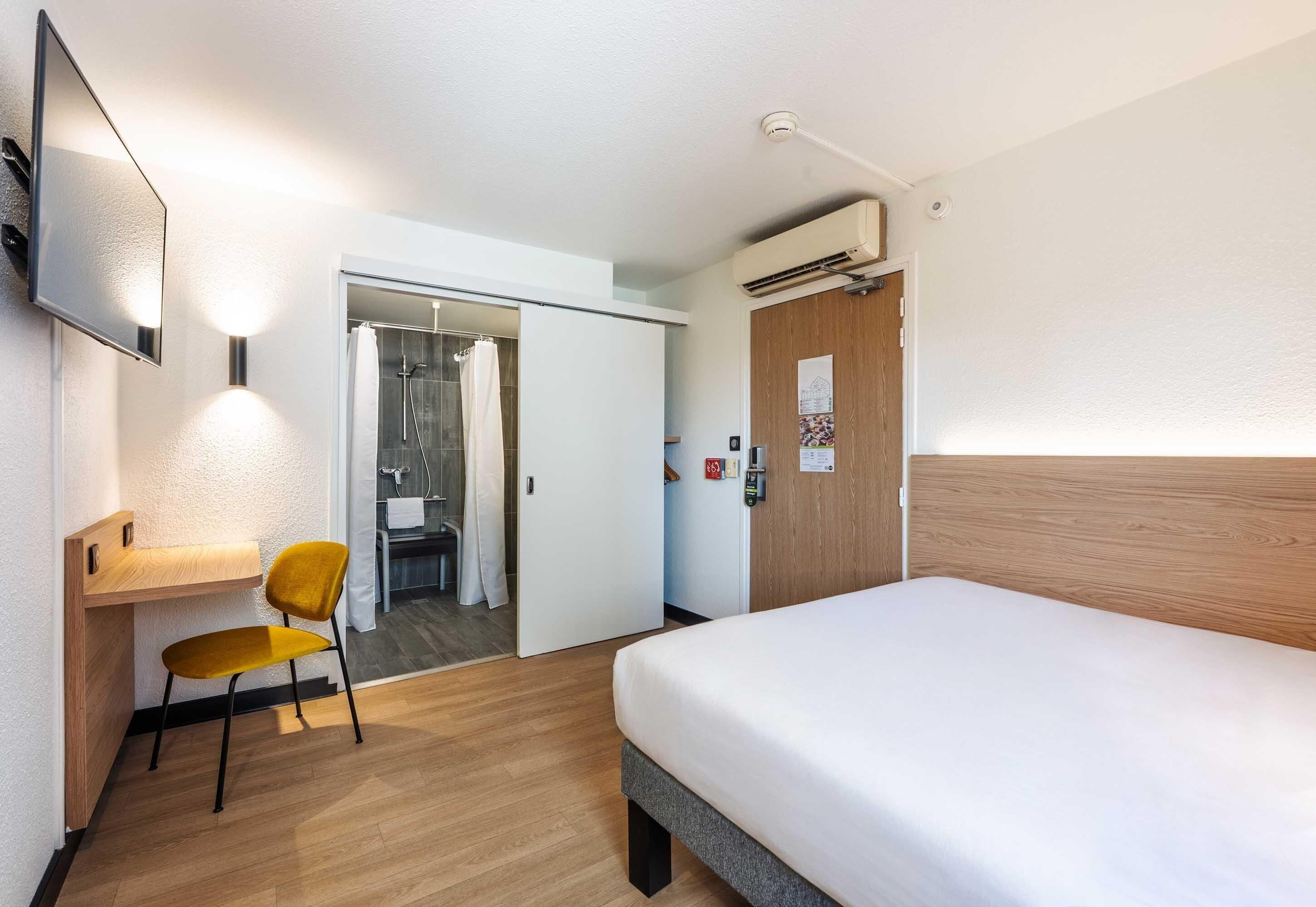 Een hotelkamer met een bed, een bureau met stoel, een televisie, een airconditioning en een houten deur.
