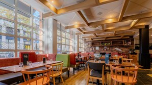A restaurant with wooden tables and chairs, large windows, and a brick wall with a menu board. - B&B Hotel Lille Roubaix Centre Grand-Place (Roubaix)