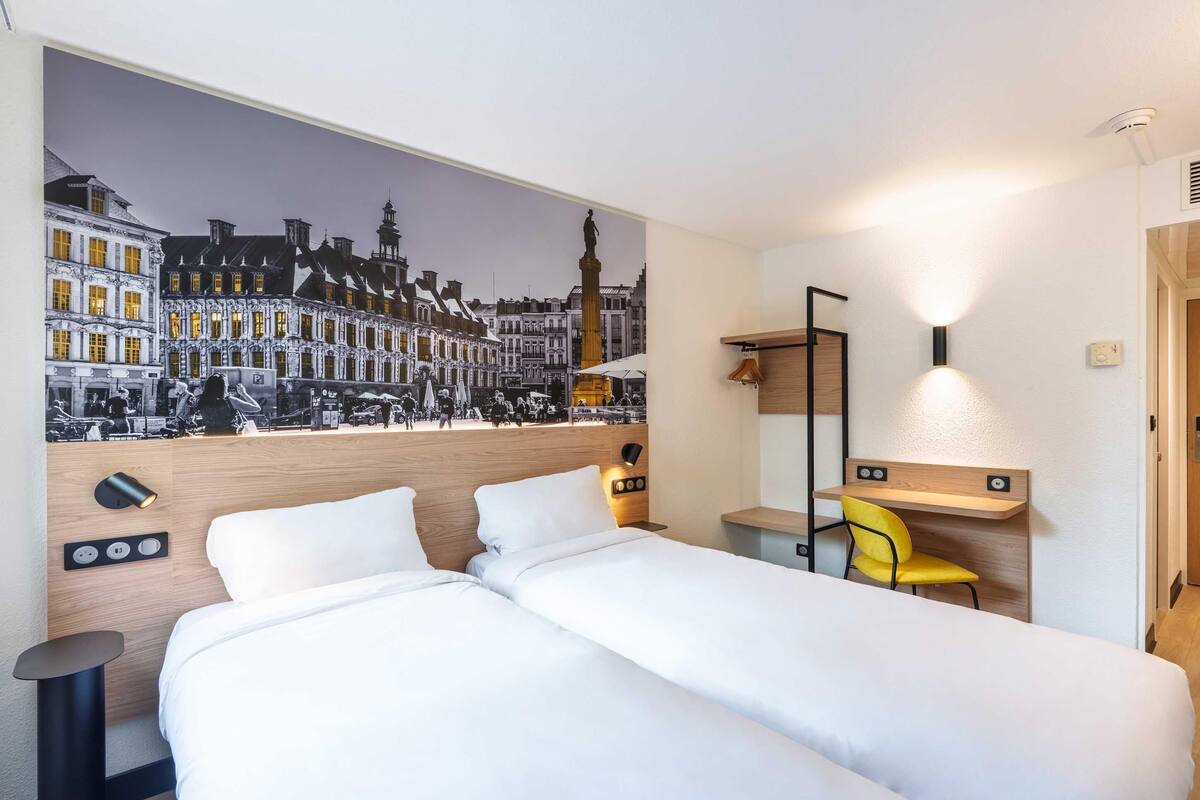 A hotel room with a large bed, a desk with a chair, a wall-mounted mirror, and a mural of a city street.