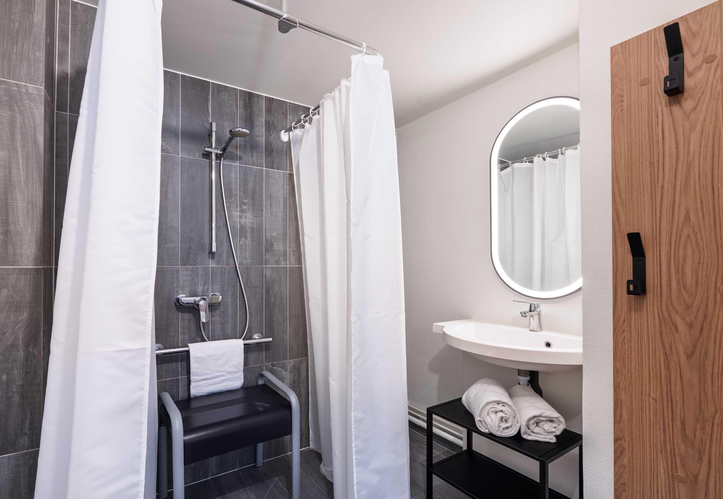 Une salle de bain moderne équipée d’une douche, d’un lavabo, d’un miroir et d’un porte-serviettes.