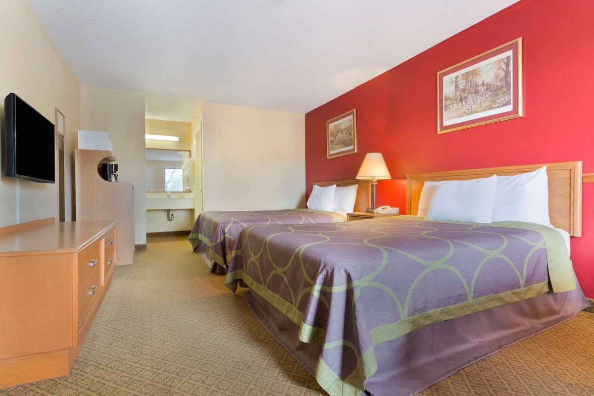 A hotel room with two beds, a TV, a desk, and a bathroom.
