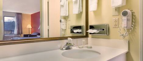 A hotel bathroom with a large mirror, white sink, towel rack, hairdryer, and a window with curtains.