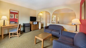 Une chambre d’hôtel avec un bureau en bois, une télévision, un canapé et une petite table.