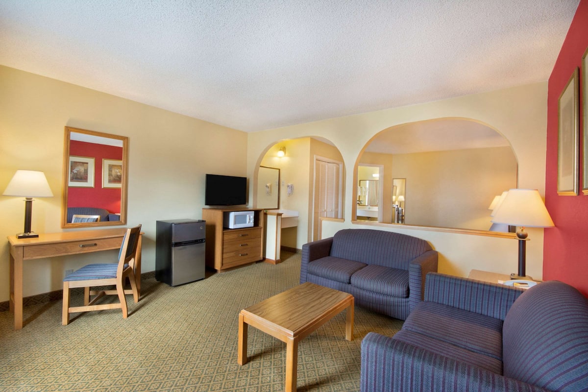A hotel room with a wooden desk, a television, a sofa, and a small table.