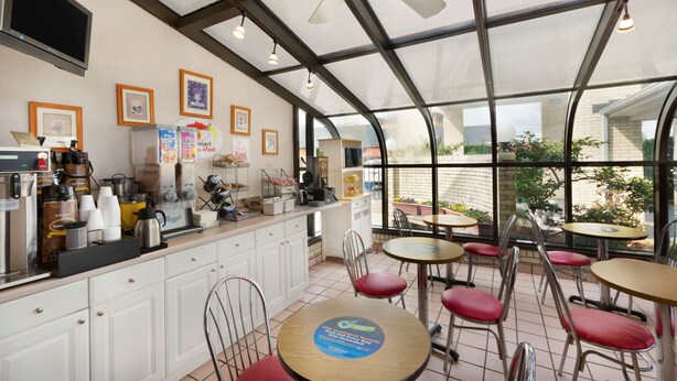 Un café doté d’une véranda en verre, de meubles blancs et de chaises rouges.