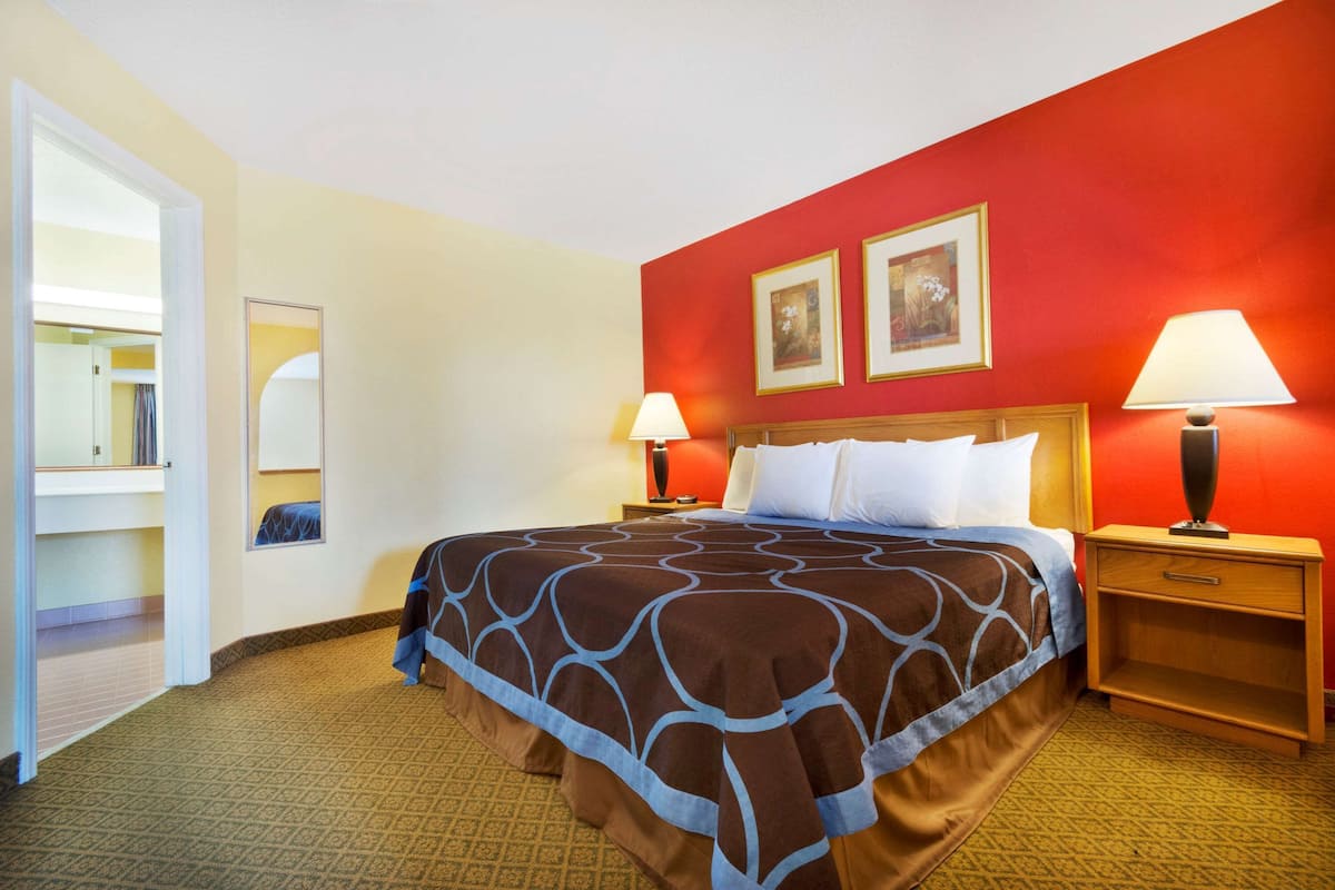 A hotel room with a large bed, two bedside tables with lamps, a mirror, and two framed pictures on the wall.