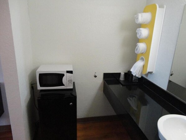 Une petite kitchenette équipée d’un four à micro-ondes et d’un appareil électroménager noir, d’un évier surmonté d’un miroir et d’un porte-serviettes avec des serviettes blanches.