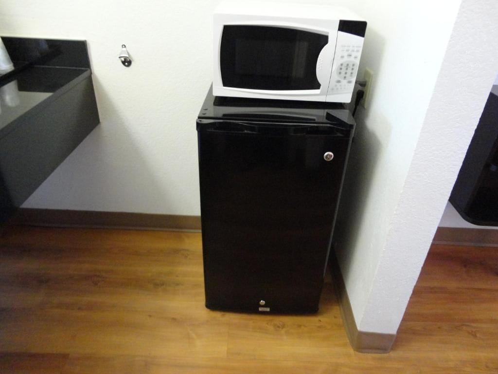 A compact black appliance with a microwave on top, located in a corner of a room with wooden flooring and a white wall.
