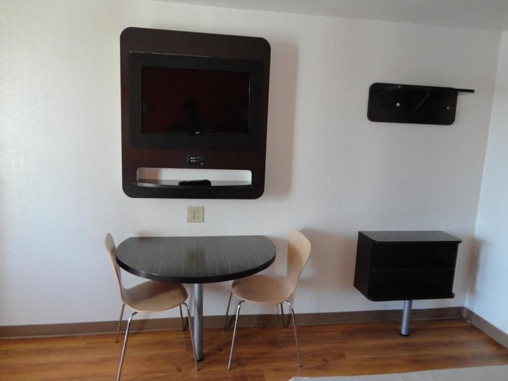 Una habitación con una mesa de comedor redonda, dos sillas, un televisor de pantalla plana en la pared y un armario negro.