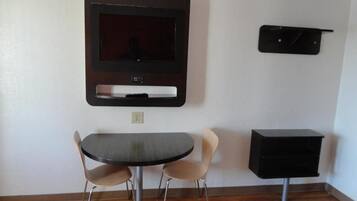 Una habitación con una mesa de comedor redonda, dos sillas, un televisor de pantalla plana en la pared y un armario negro.