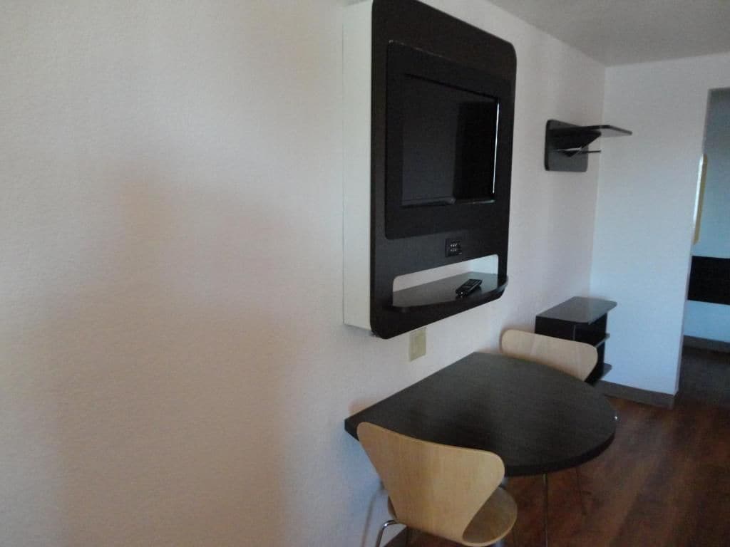Une chambre moderne avec un téléviseur à écran plat fixé au mur, une petite table avec une chaise et un canapé de couleur sombre.