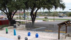 A parking lot with a fenced area, trees, and a gazebo. - Motel 6 Round Rock, TX (Round Rock)