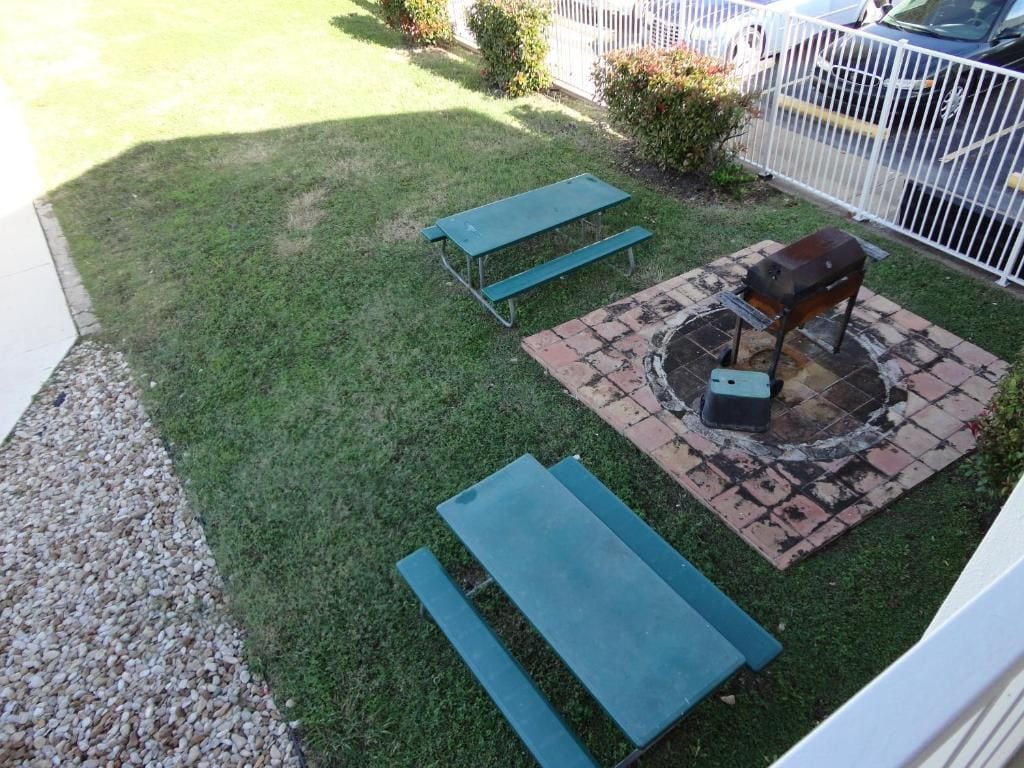 Un patio con mesa, bancos, una fogata y una cerca blanca.