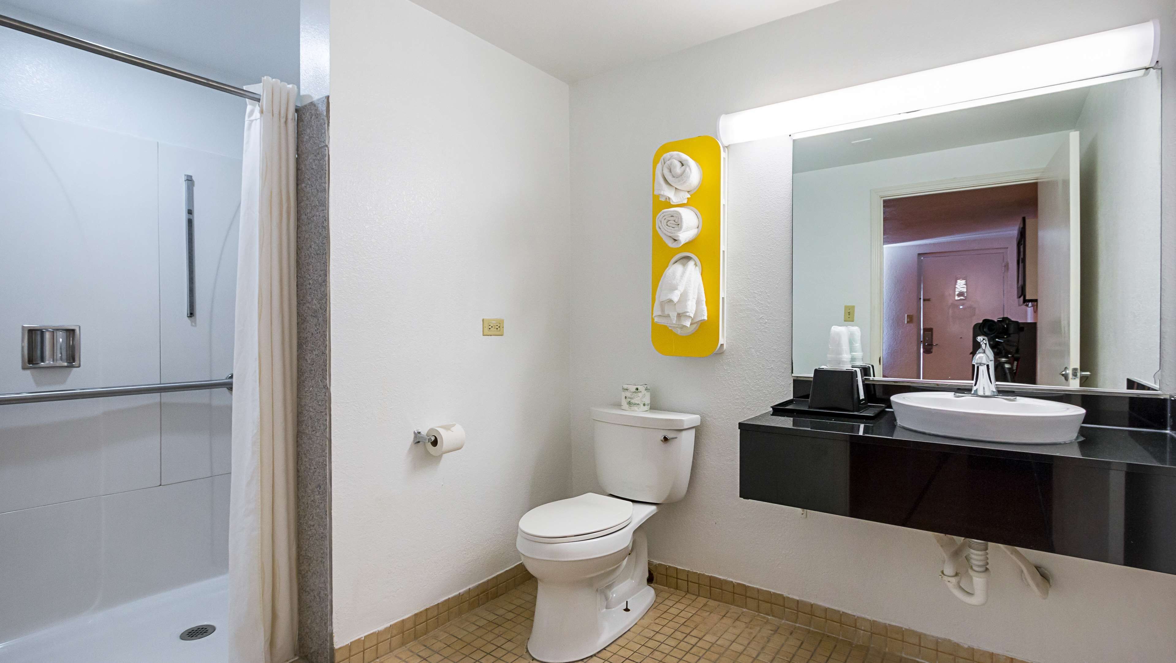 Un baño con ducha, inodoro, lavamanos y espejo con un toallero amarillo.