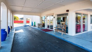 A covered outdoor area with a bench, a red mat, and a glass door entrance. - Motel 6 Round Rock, TX (Round Rock)