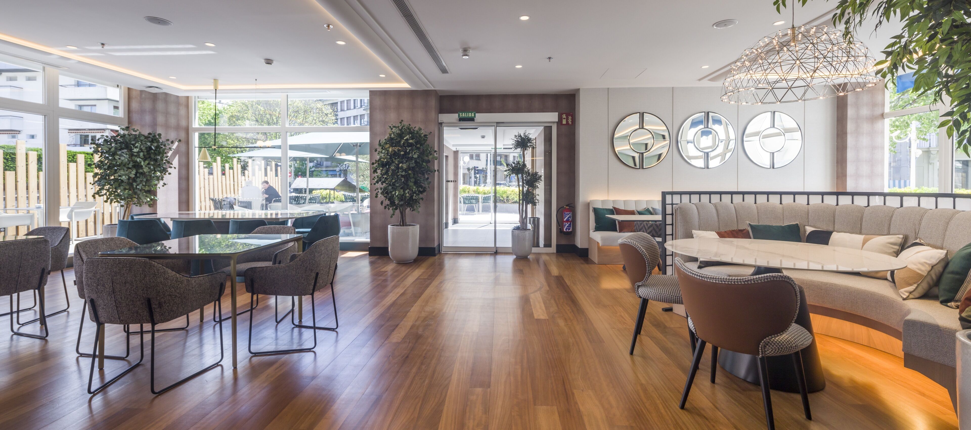 Un moderno vestíbulo de hotel con una zona de estar, un mostrador de recepción y grandes ventanales que ofrecen vistas al exterior.