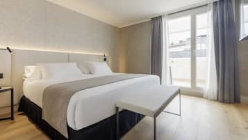 Habitación de hotel moderna con una cama grande, mesita de noche y vistas de la ciudad a través de la ventana.