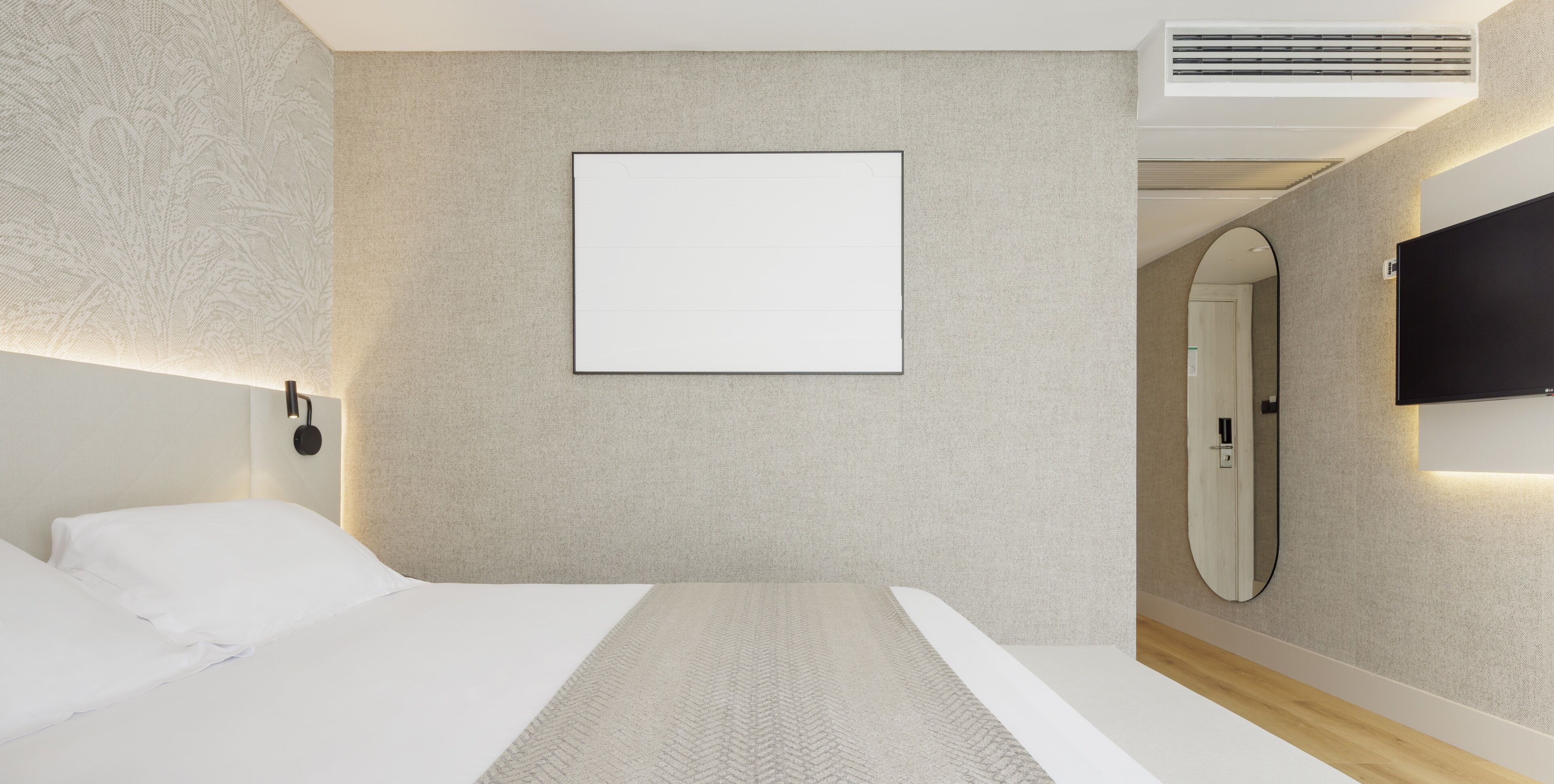 A modern hotel room with a large bed, a mounted TV, a wall-mounted mirror, and a blank framed picture.