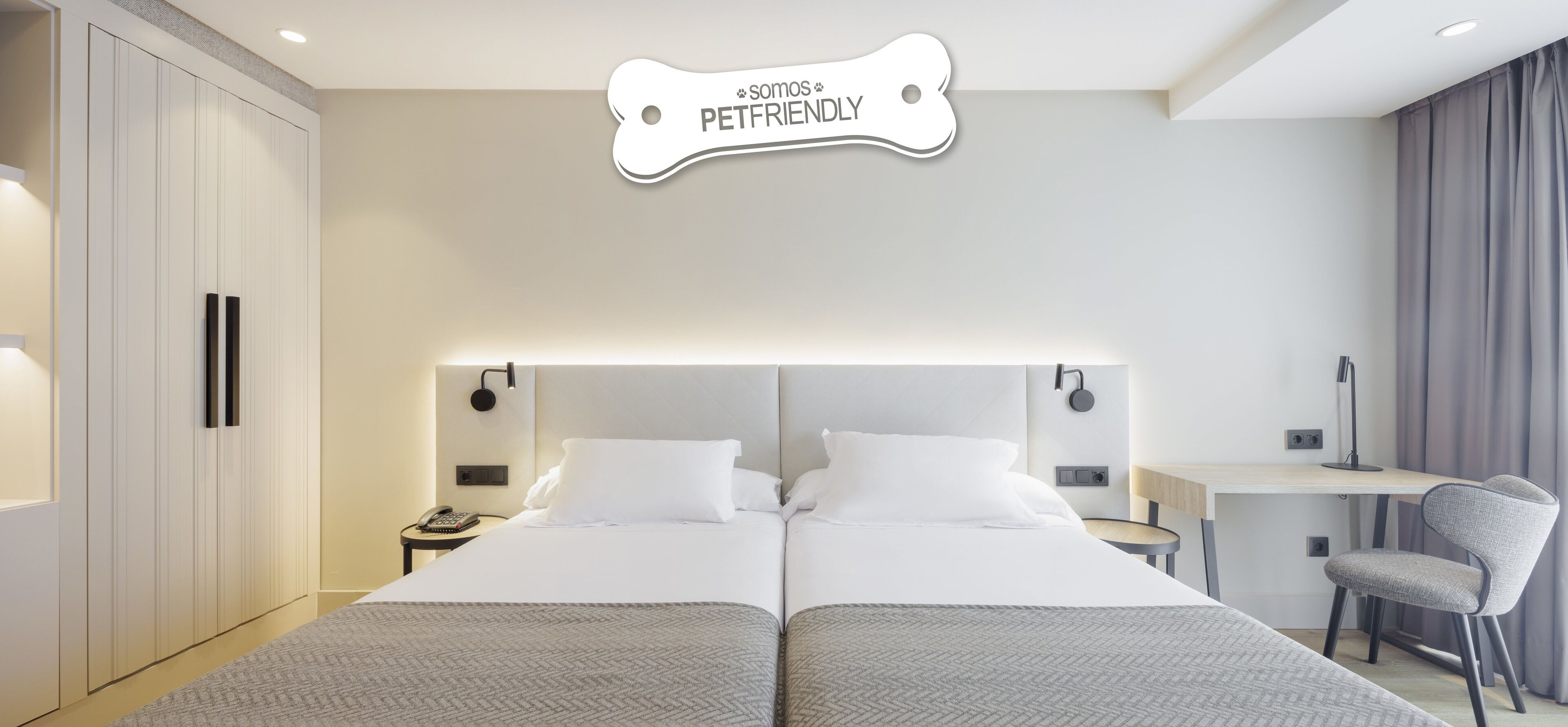 Quarto de hotel com cama de casal, mesas de cabeceira, escrivaninha e uma cadeira.