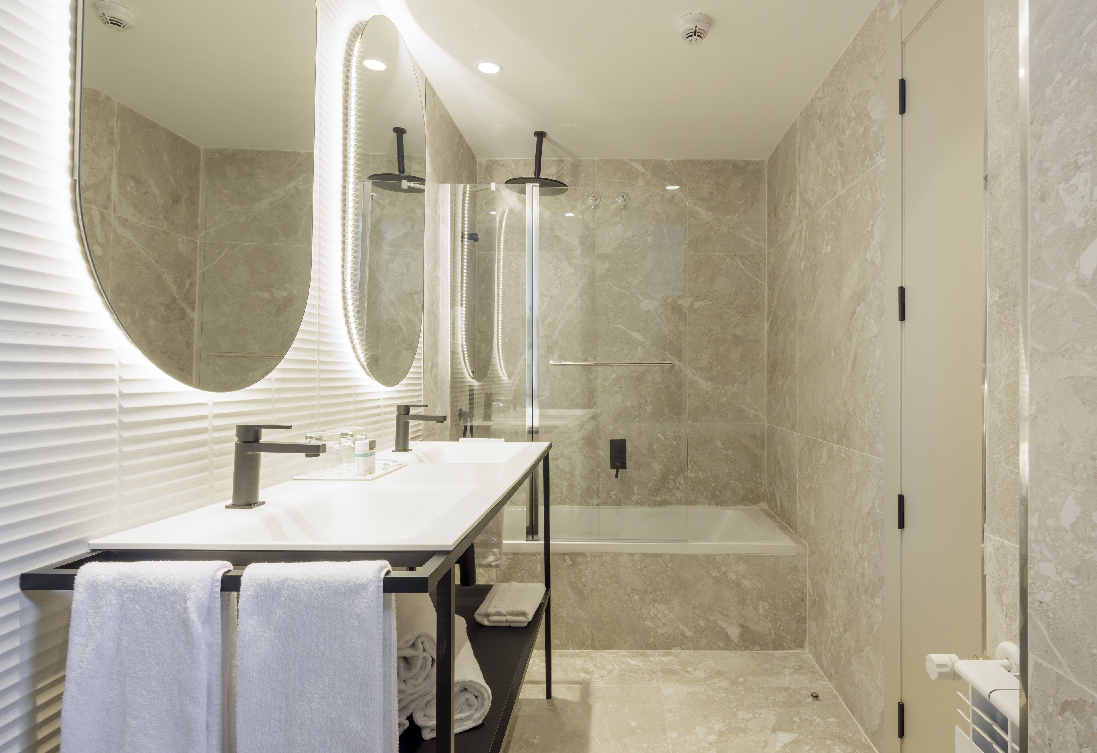 A modern bathroom with a double sink, a large mirror, a glass-enclosed shower, and a bathtub.