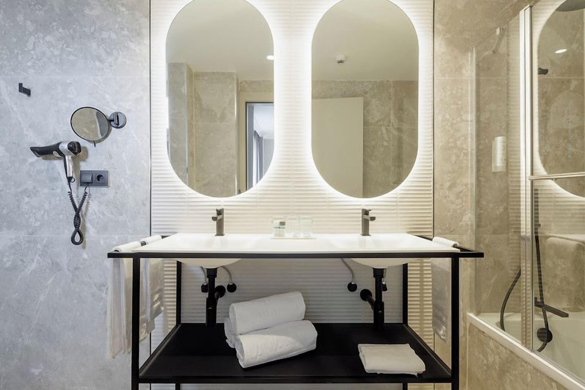 A modern bathroom with a double sink, large mirrors, and a shower area.