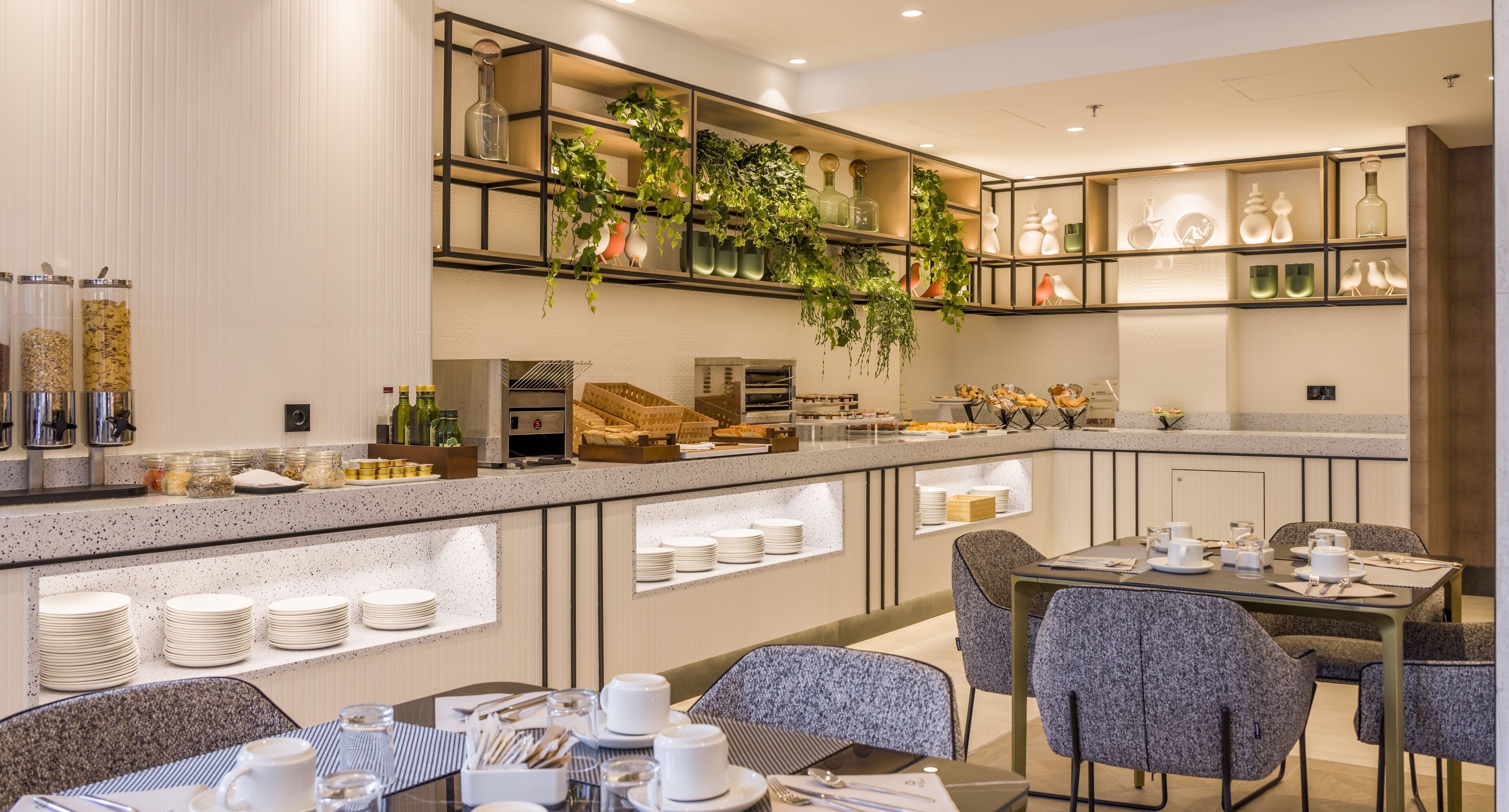 Un comedor de hotel moderno con un sistema de buffet, disposición de mesas y plantas decorativas.