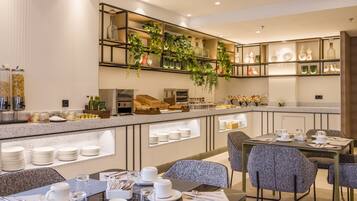 Un comedor de hotel moderno con un sistema de buffet, disposición de mesas y plantas decorativas.