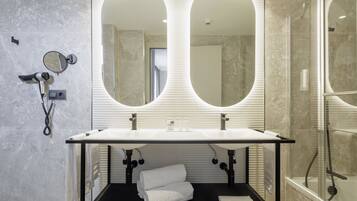 Un baño moderno con tocador doble lavamanos, un secador de pelo, un perchero para toallas y una ducha con mampara de vidrio.
