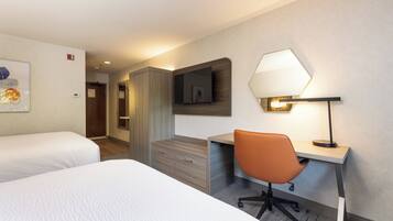 Une chambre d’hôtel avec deux lits, un bureau avec une chaise, un miroir et une lampe.