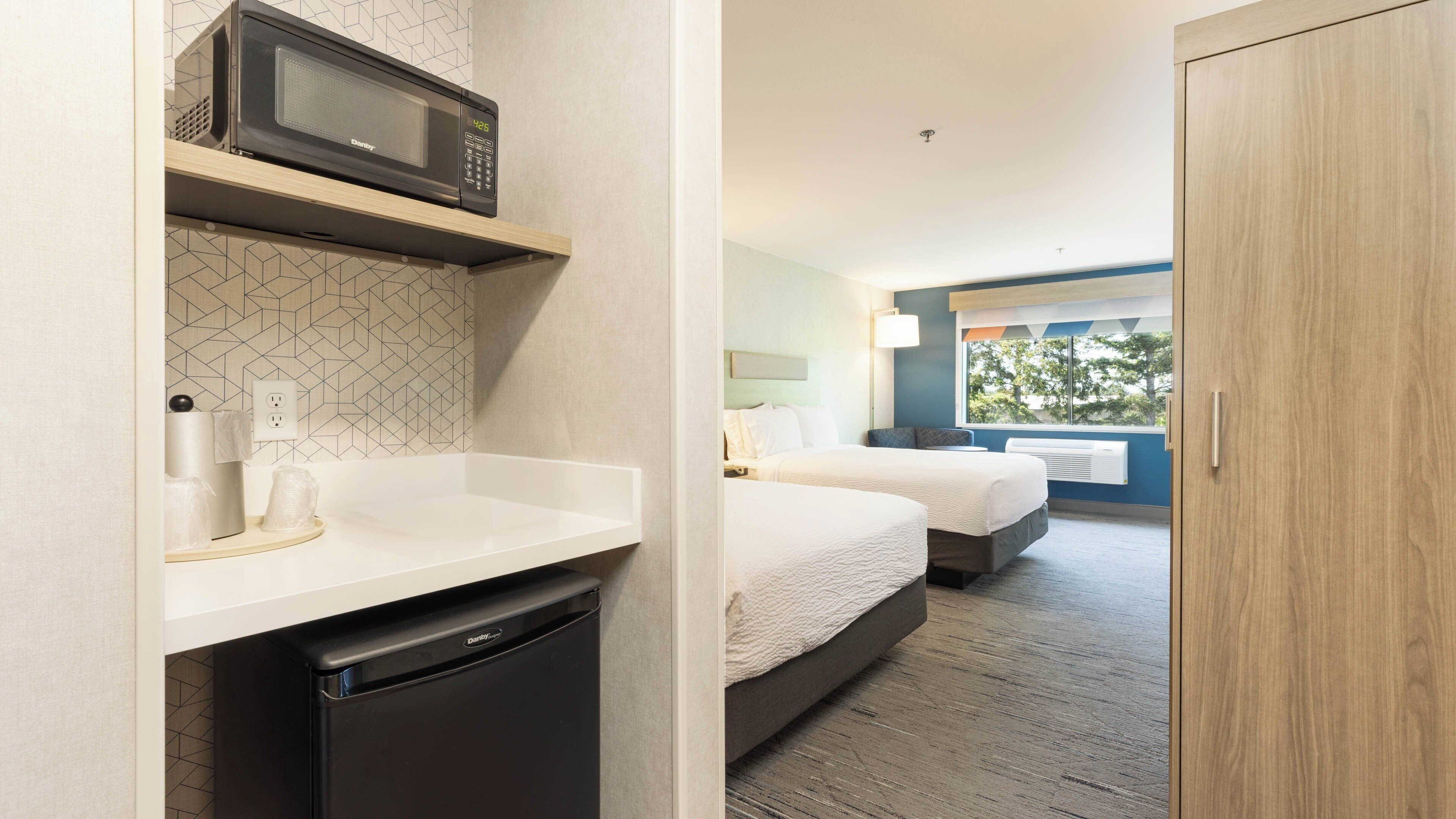 A hotel room with a microwave, a sink, a compact dishwasher, two beds, and a window with a view.