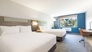 A hotel room with two beds, a desk, a chair, a window with a view, and a wall-mounted phone.