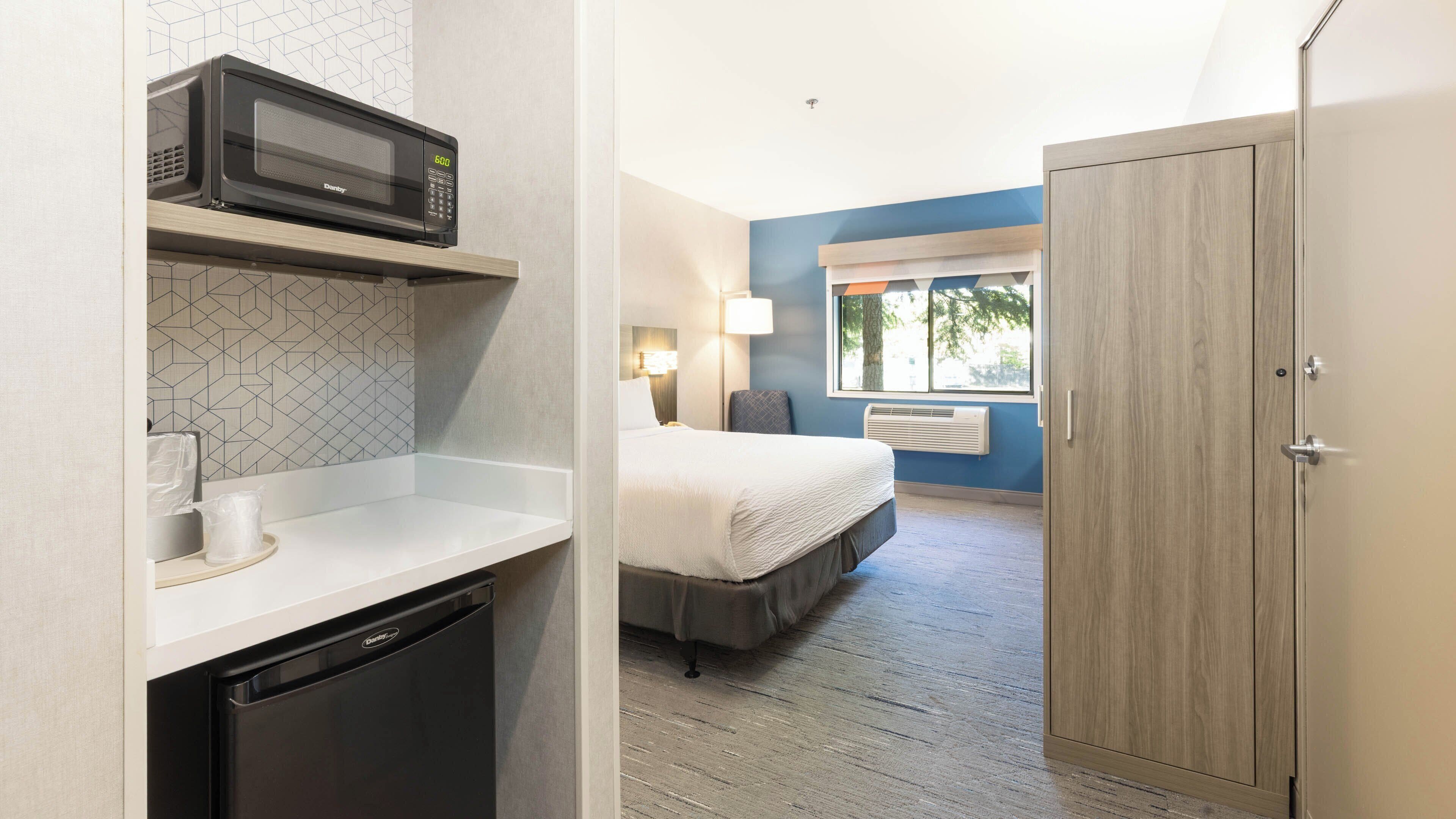 A hotel room with a bed, a microwave, a small kitchen area, and a wardrobe.