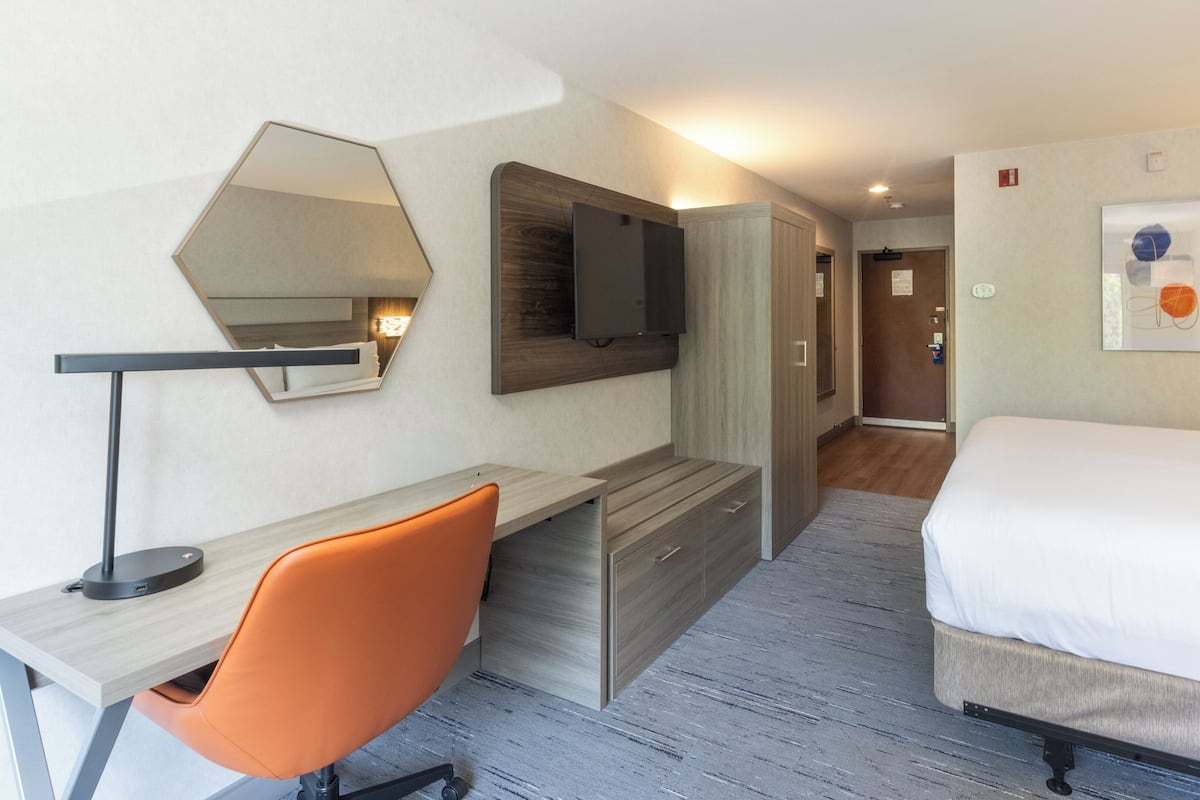 A hotel room with a bed, a desk with a chair, a TV, and a mirror.