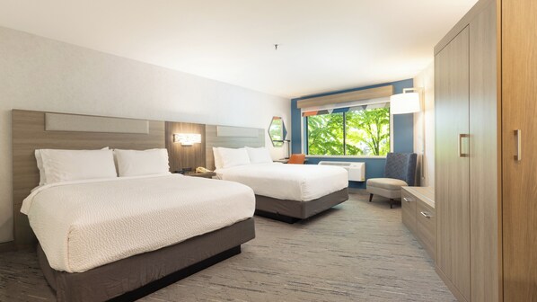 A hotel room with two beds, a desk, a chair, a wardrobe, and a window with a view of trees.