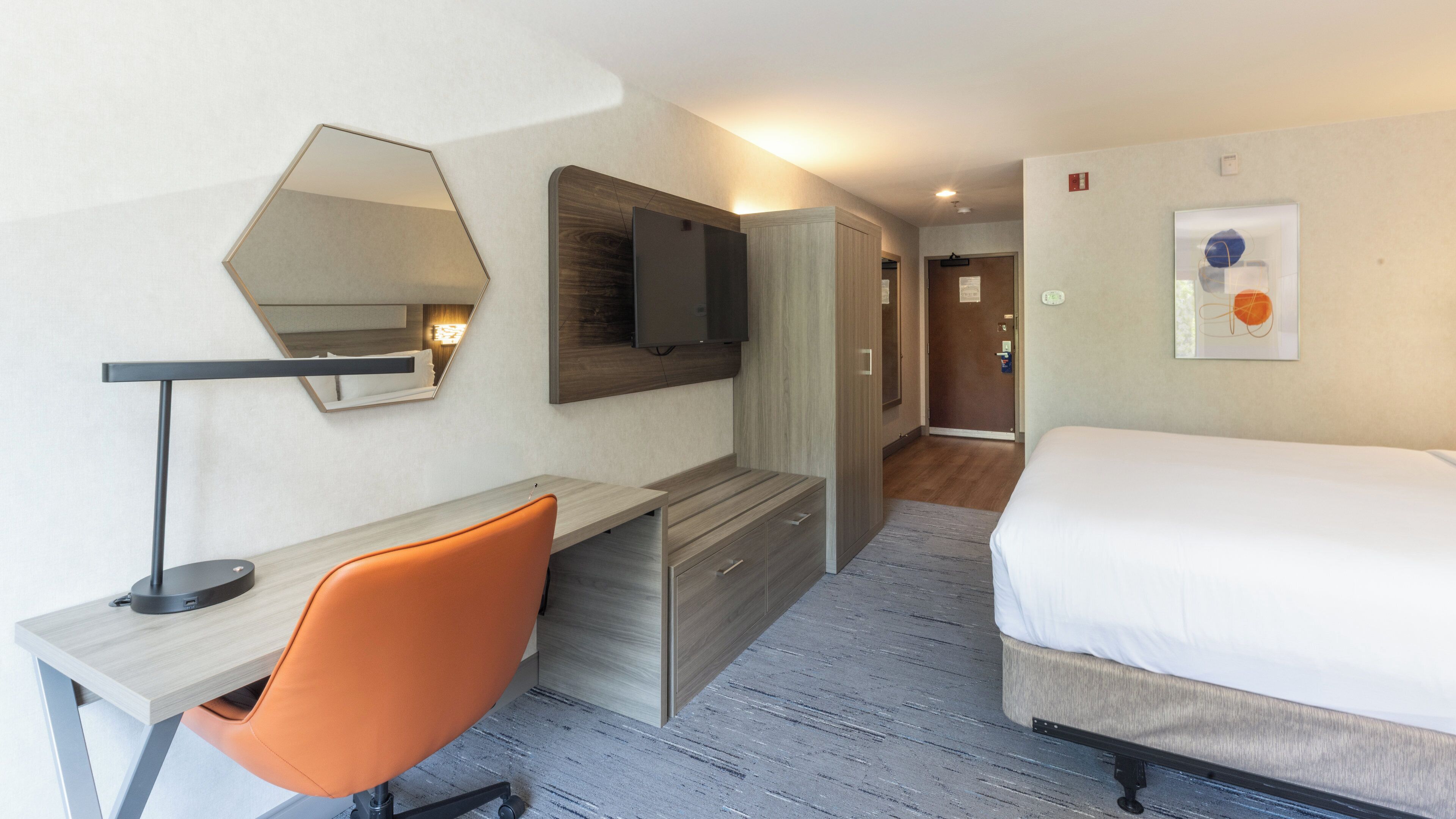 Une chambre d’hôtel comprenant un lit, un bureau avec une chaise, une télévision et un miroir.