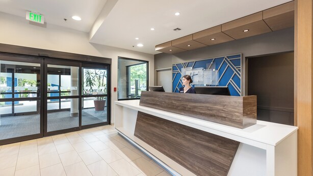 A hotel reception area with a modern design, including a reception desk, a large window, and an exit sign.