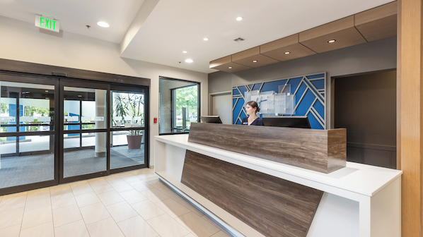 A hotel reception area with a modern design, including a reception desk, a large window, and an exit sign.