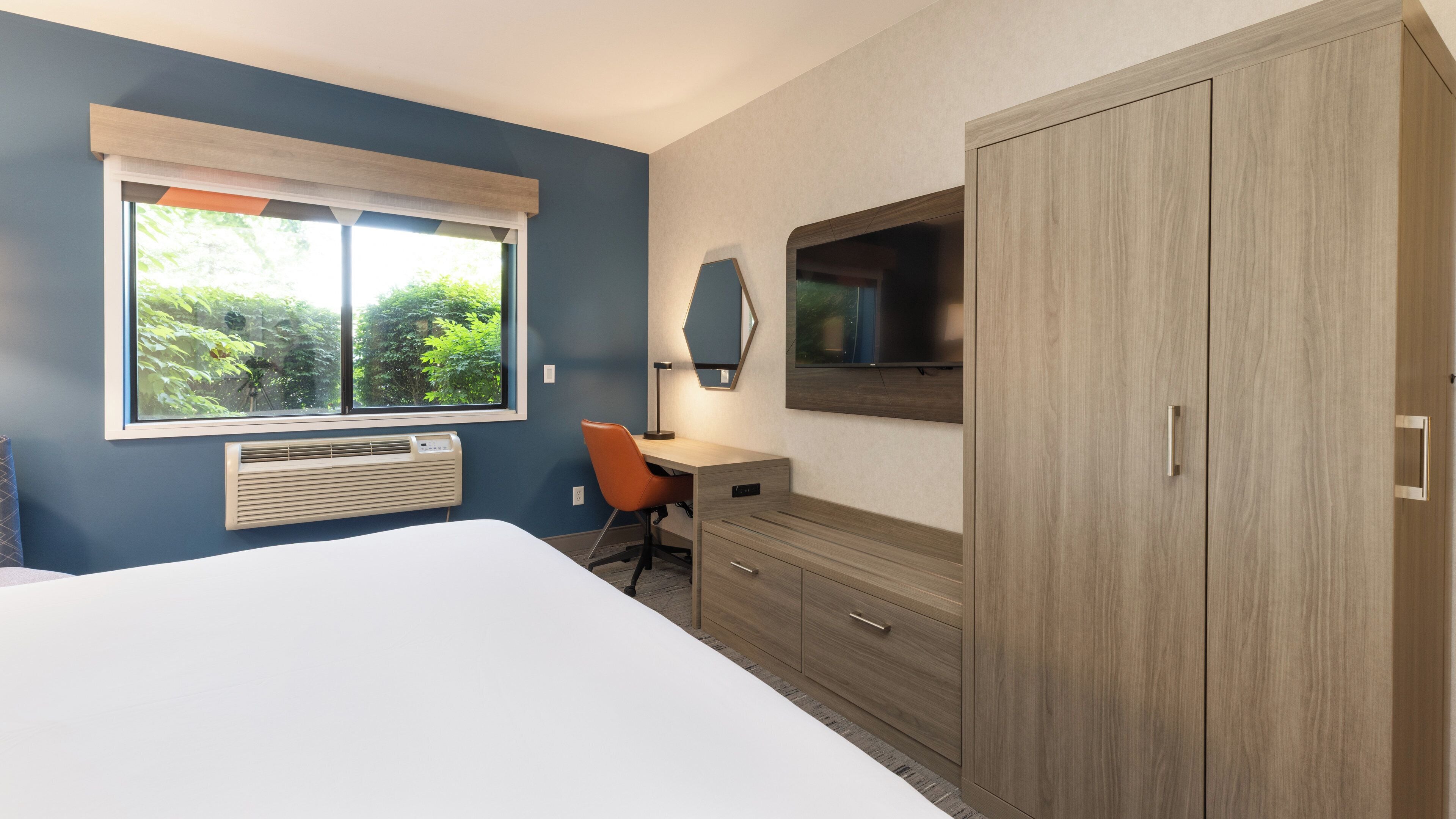 Un dormitorio con cama, escritorio, silla, televisor y armario.