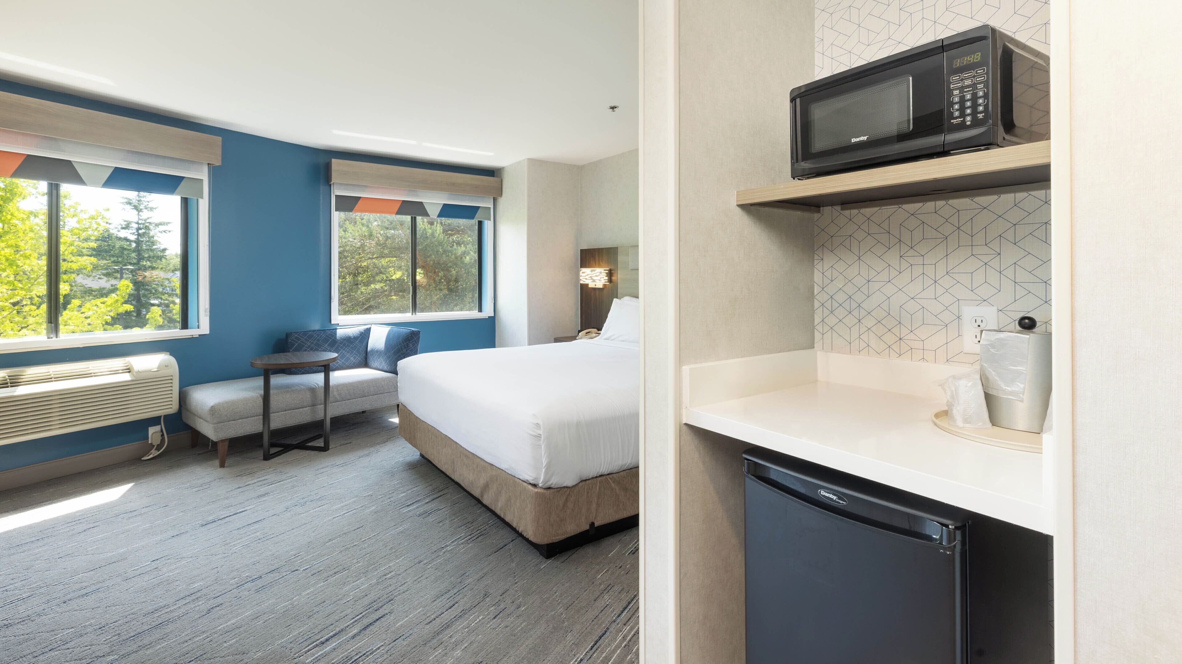 A hotel room with a bed, a seating area, a microwave, and a small kitchenette.