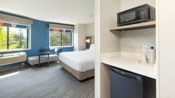 A hotel room with a bed, a seating area, a microwave, and a small kitchenette.
