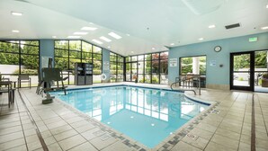 A large indoor swimming pool with clear glass walls, a lifeguard chair, and a pool rule sign.