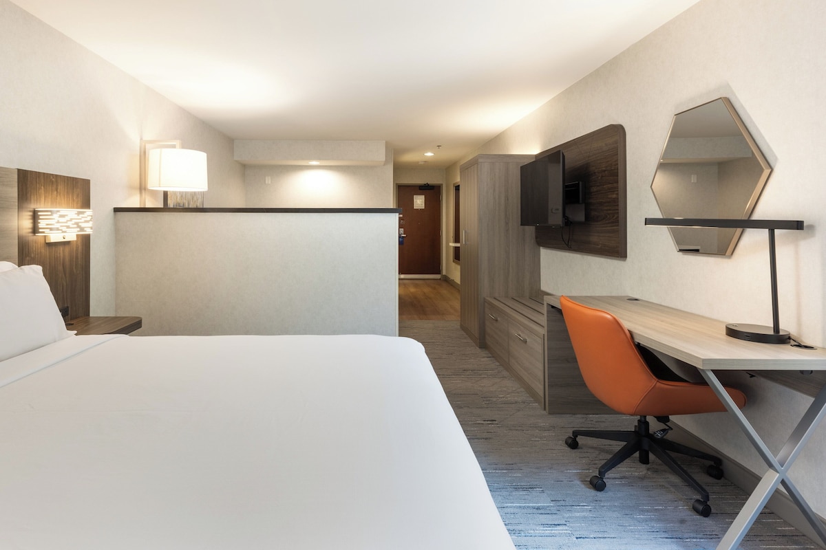 A hotel room with a large bed, a desk with a chair, a TV, and a mirror.