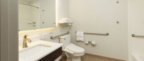 A modern bathroom with a sink, toilet, and shower. It includes a mirror, towel rack, and handrails.